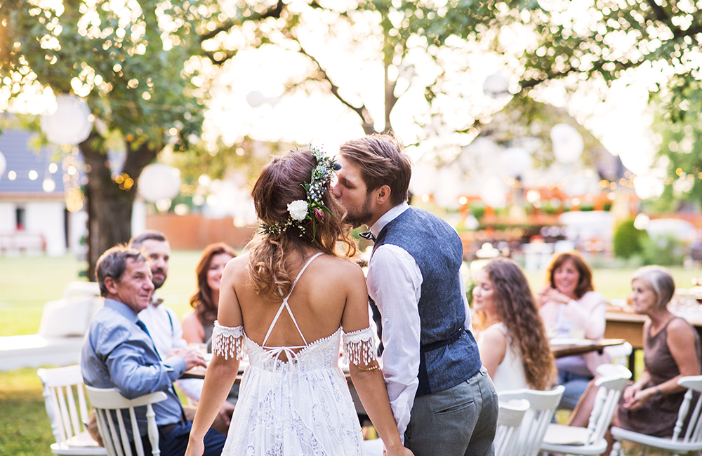 Bride and groom kissing at wedding reception outside in the backyard.